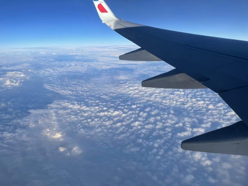 Ala de avión por encima de la capa de nubes de apariencia pequeña y cielo azul sobre el horizonte lejano.