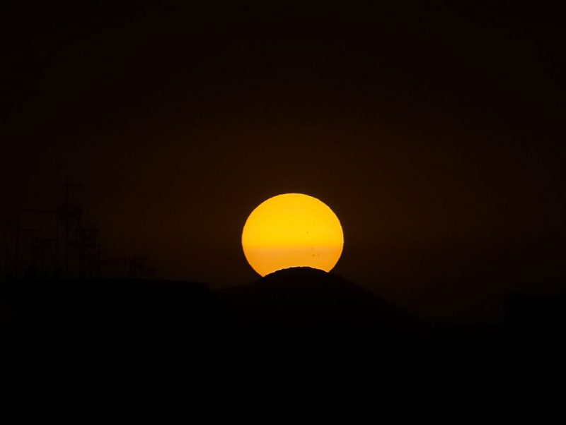 Sol amarillo con un tono naranja en el medio.  La parte inferior de la esfera está oculta detrás de una colina.