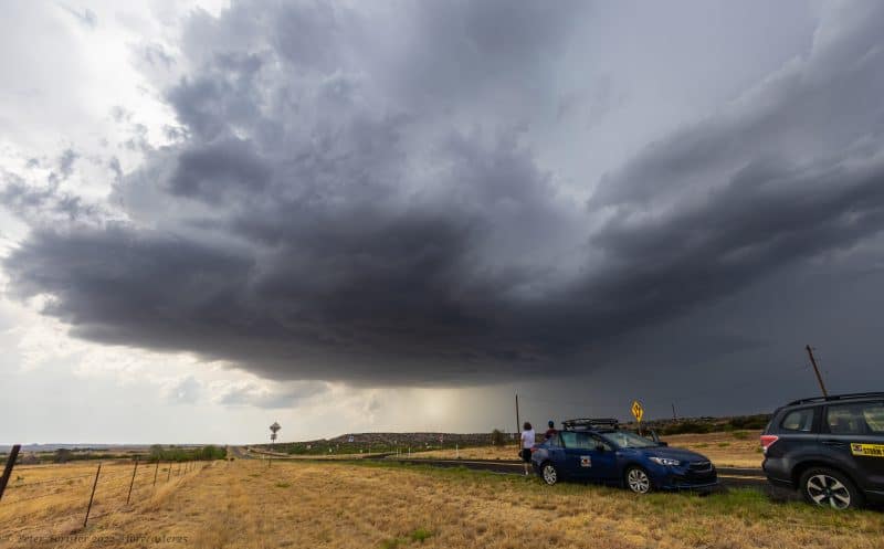 Persiguiendo tormentas: personas paradas junto a dos autos en una carretera solitaria observando nubes oscuras.