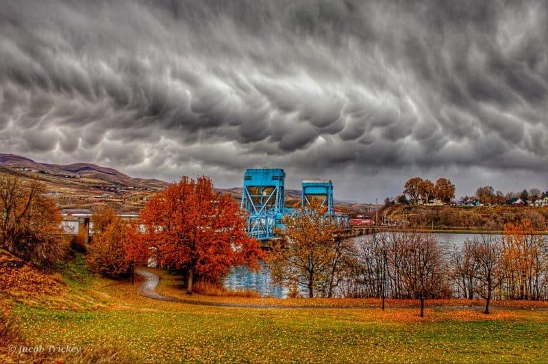 Nubes bajas de color gris oscuro que se abultan hacia abajo sobre un puente azul que cruza un río.