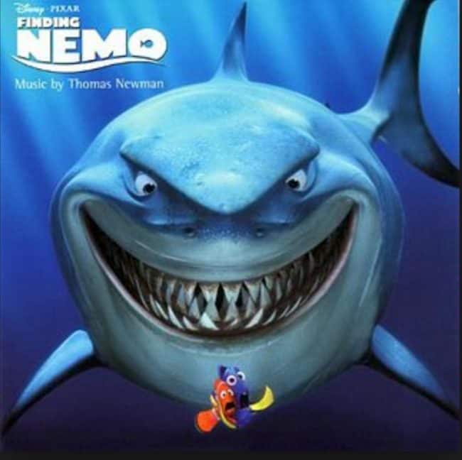 Tiburón de dibujos animados sonriente de la película Buscando a Nemo con 2 peces pequeños al frente.