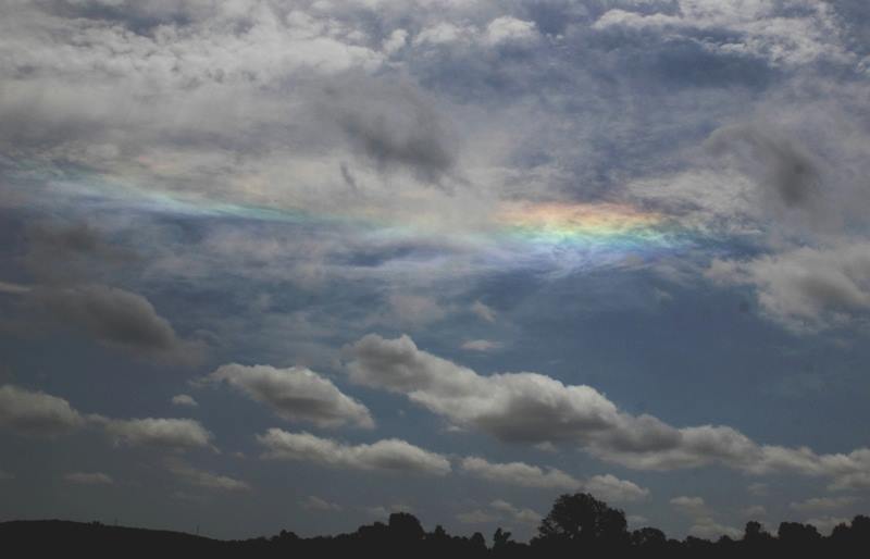 Cielo con nubes hinchadas, una raya corta de arcoíris a mitad de camino.